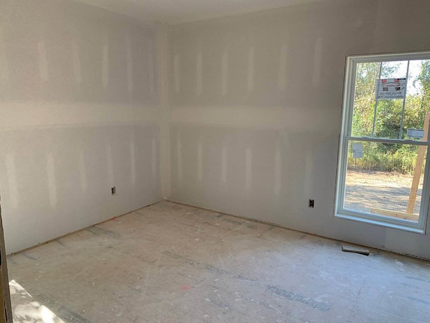 Bright room with smooth white walls, white floor, large window with a sign, and a door; minimal finishes and clean plaster surfaces.