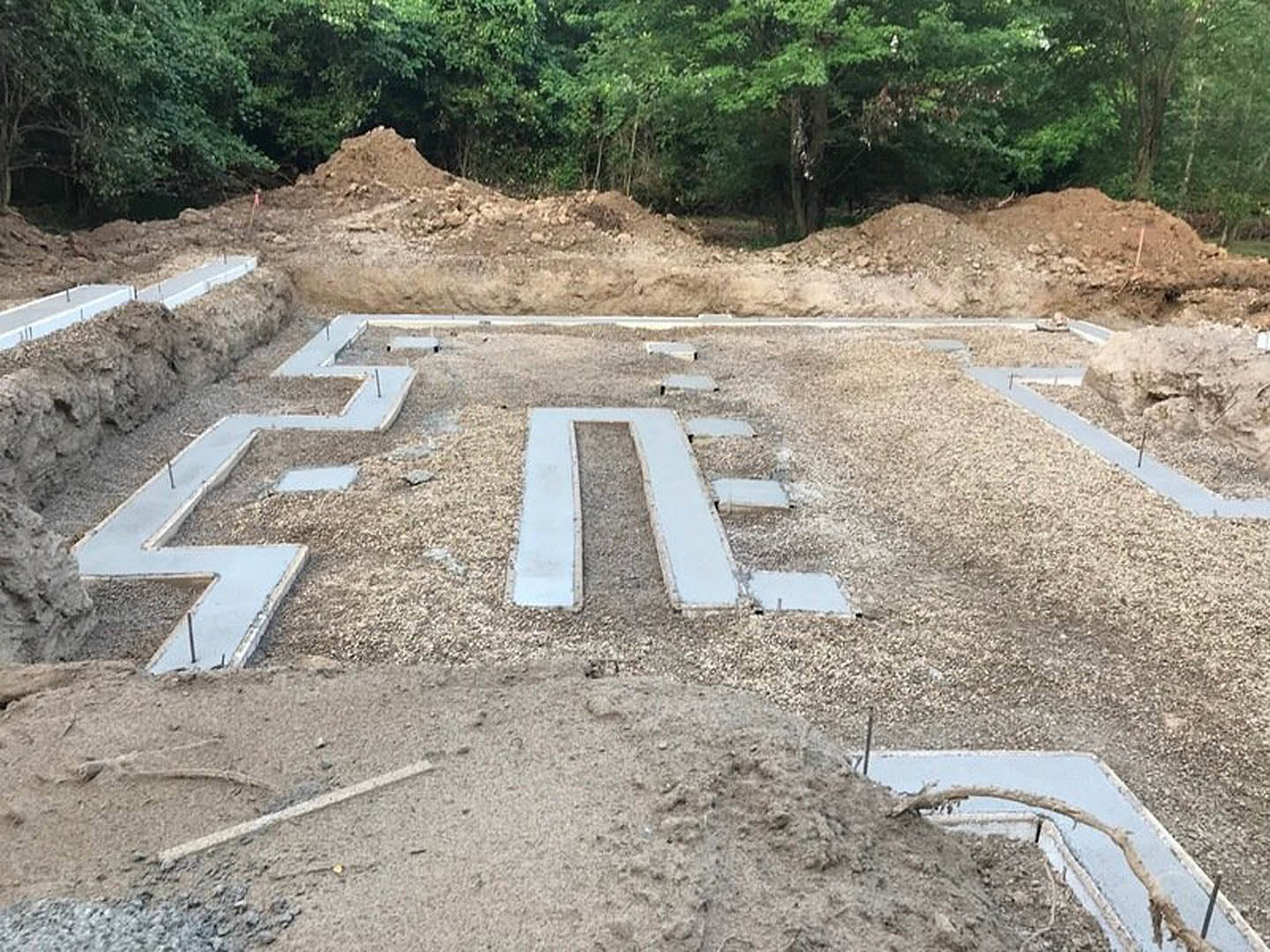 Rectangular concrete slab surrounded by gravel and dirt, construction site bordered by trees and soil, broken mirror lying on the ground