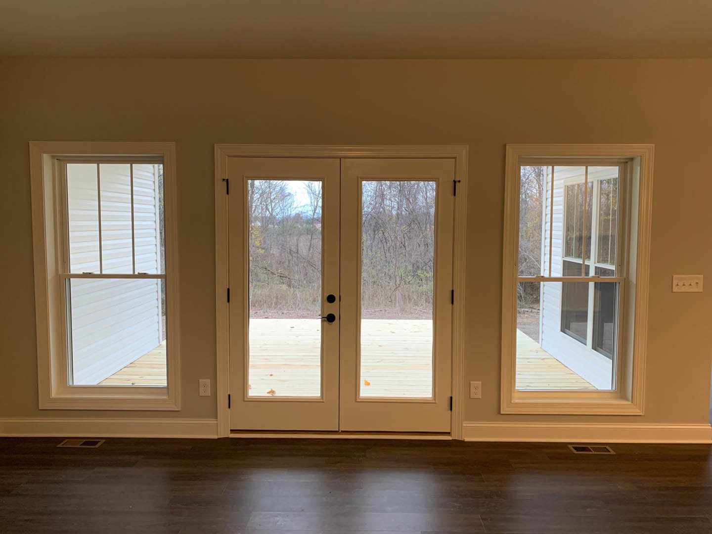 Wood-floored room featuring double glass-paneled doors opening to a deck, white-framed window, and neutral walls