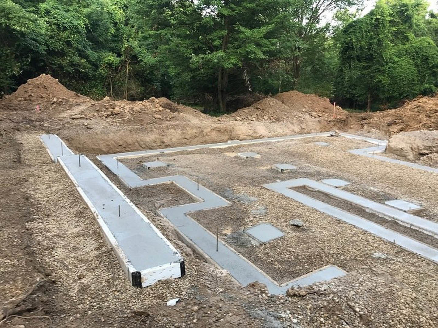 Concrete foundation slabs surrounded by dirt and scattered trees at a residential construction site
