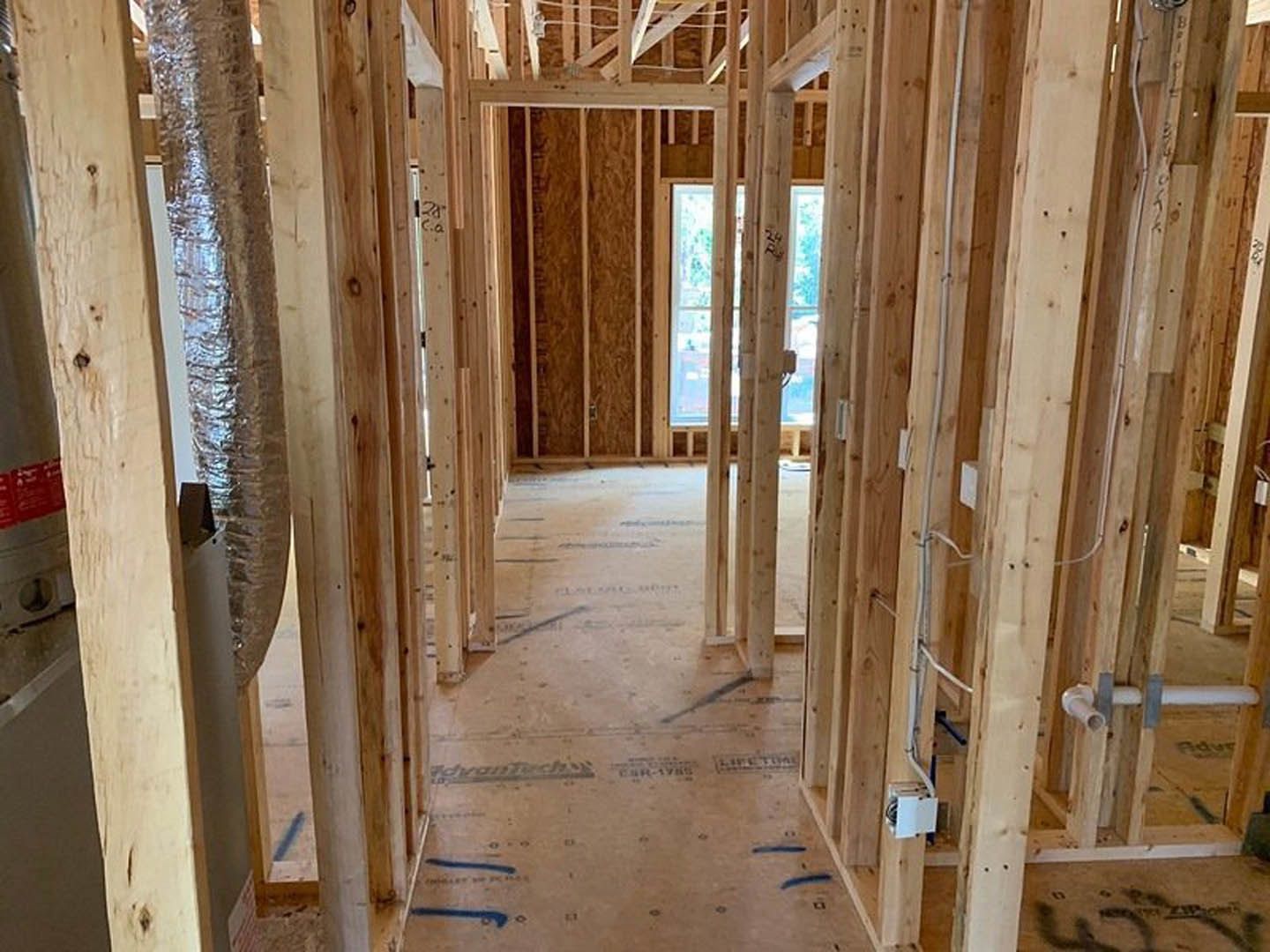 Exposed wood framing with beams and planks, partially installed window and door, red construction sign with white text, building insulation visible indoors