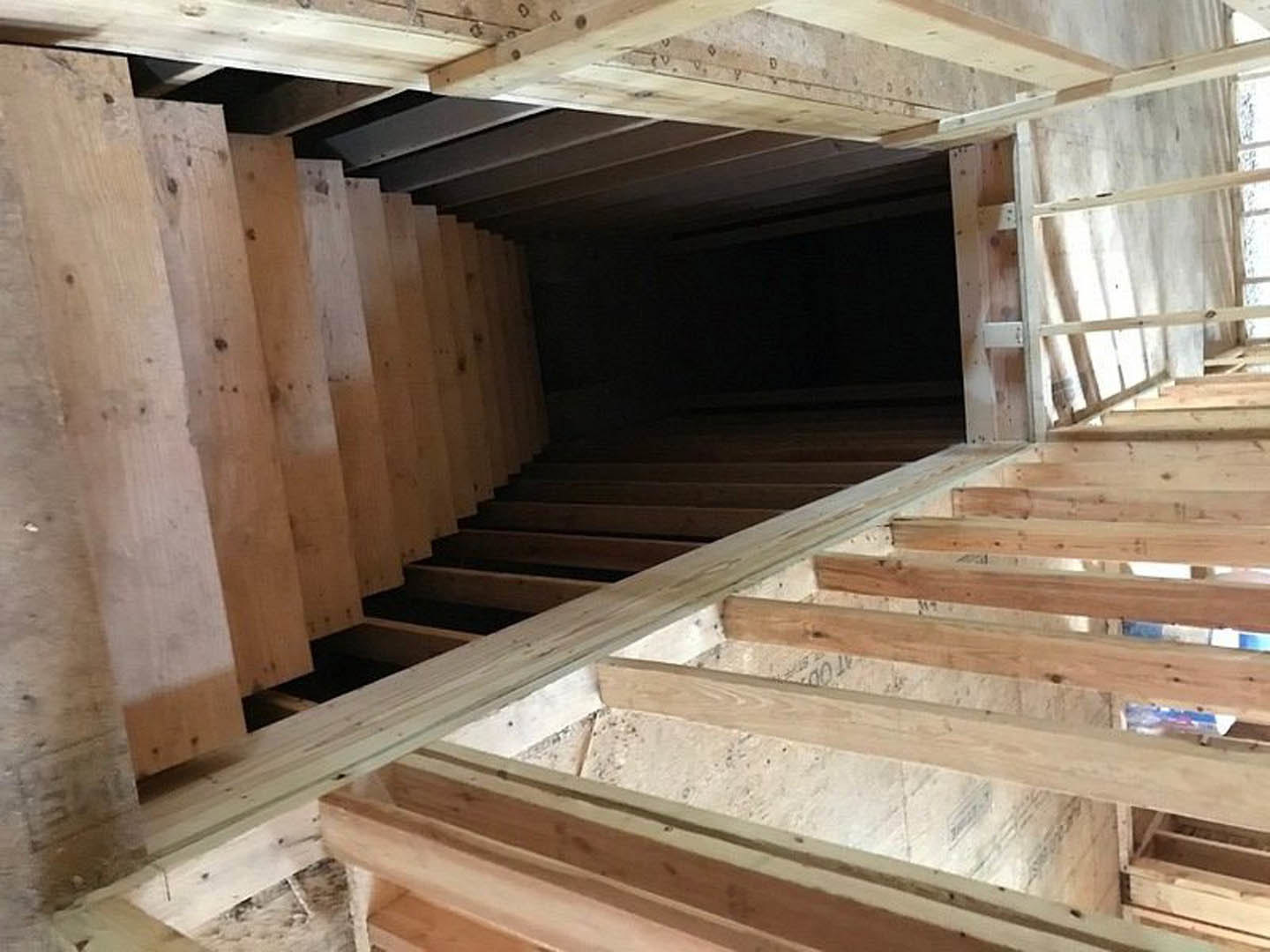 Wooden staircase with natural finish ascending beside white walls, exposed beams, and window frame in a modern residential interior.