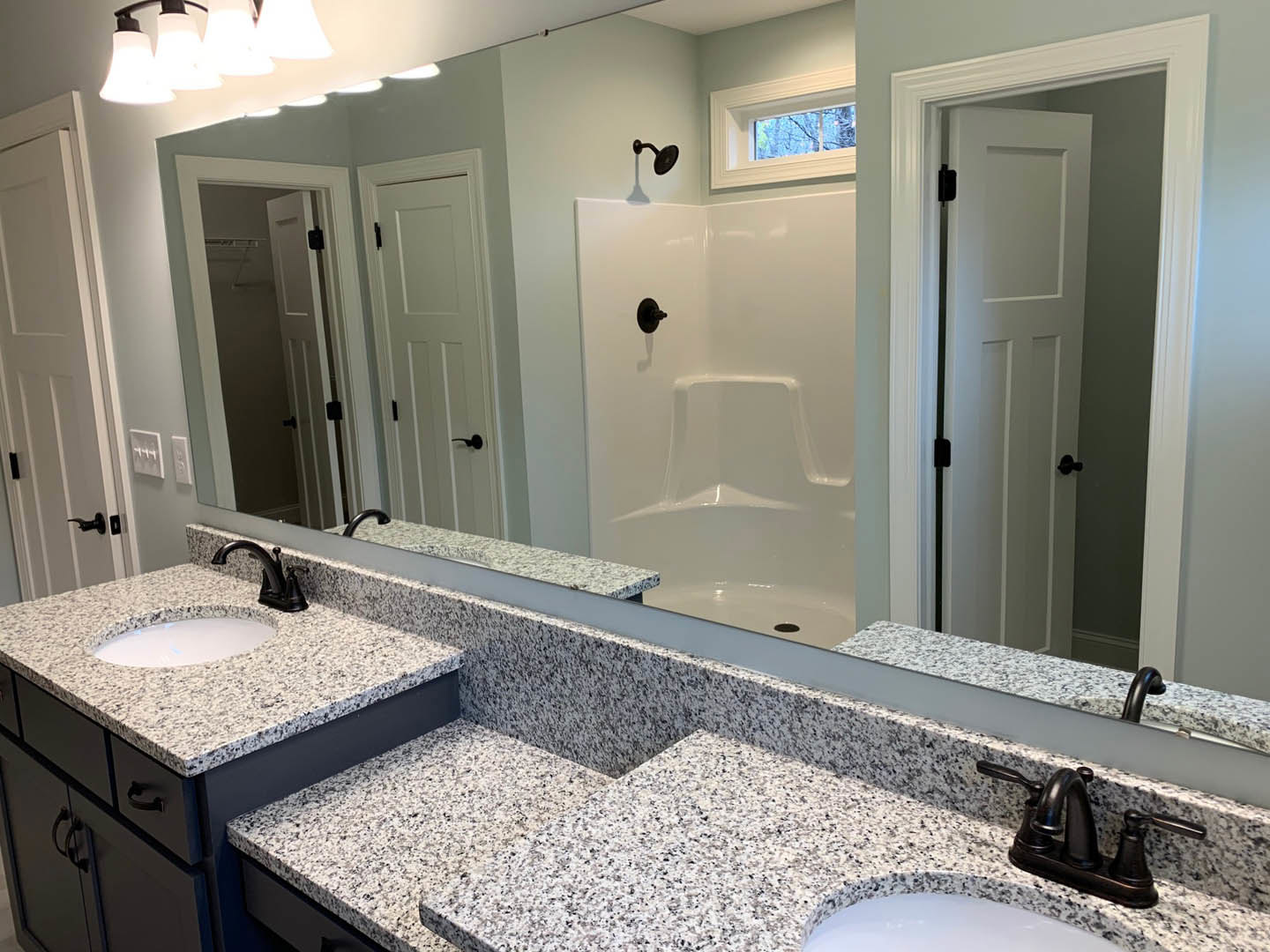 Bathroom with a wide framed mirror above dual white sinks featuring blue specks, black faucet fixtures, light gray tile backsplash, white bathtub with black hardware, and a