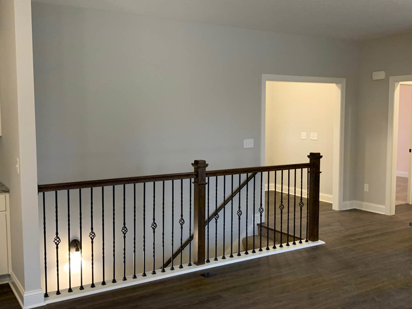 Wood staircase with black metal railing, white plaster walls, dark hardwood flooring, white door with black knob, wall sconce lighting, person standing near large window in