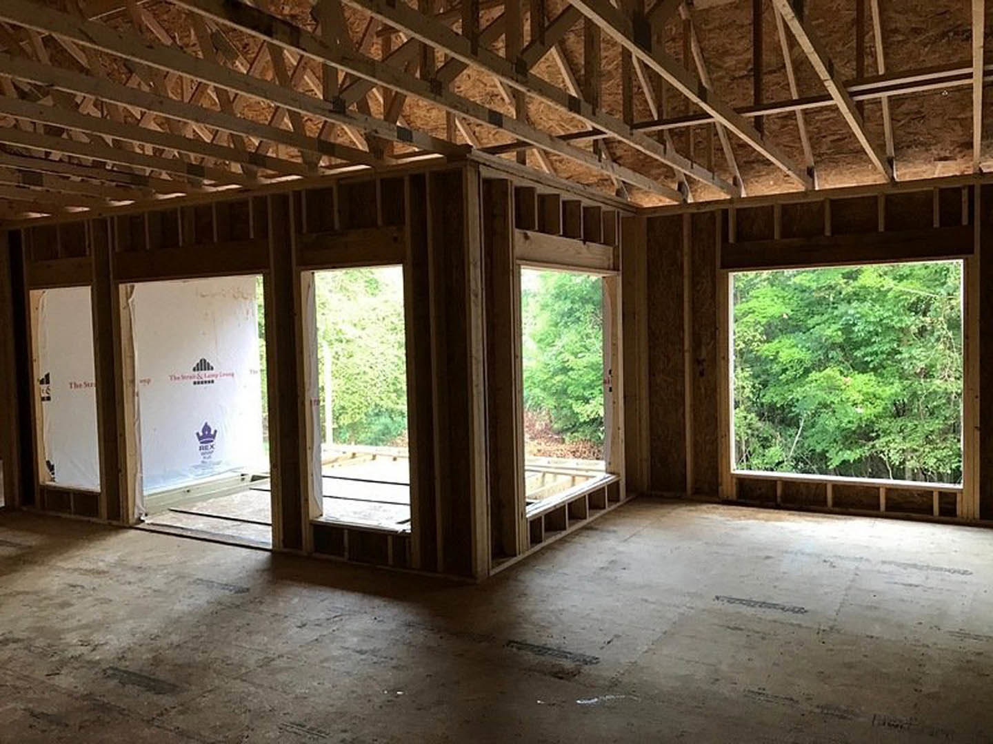 Spacious room with large windows, exposed wood ceiling beams, concrete floor, and views of trees outside