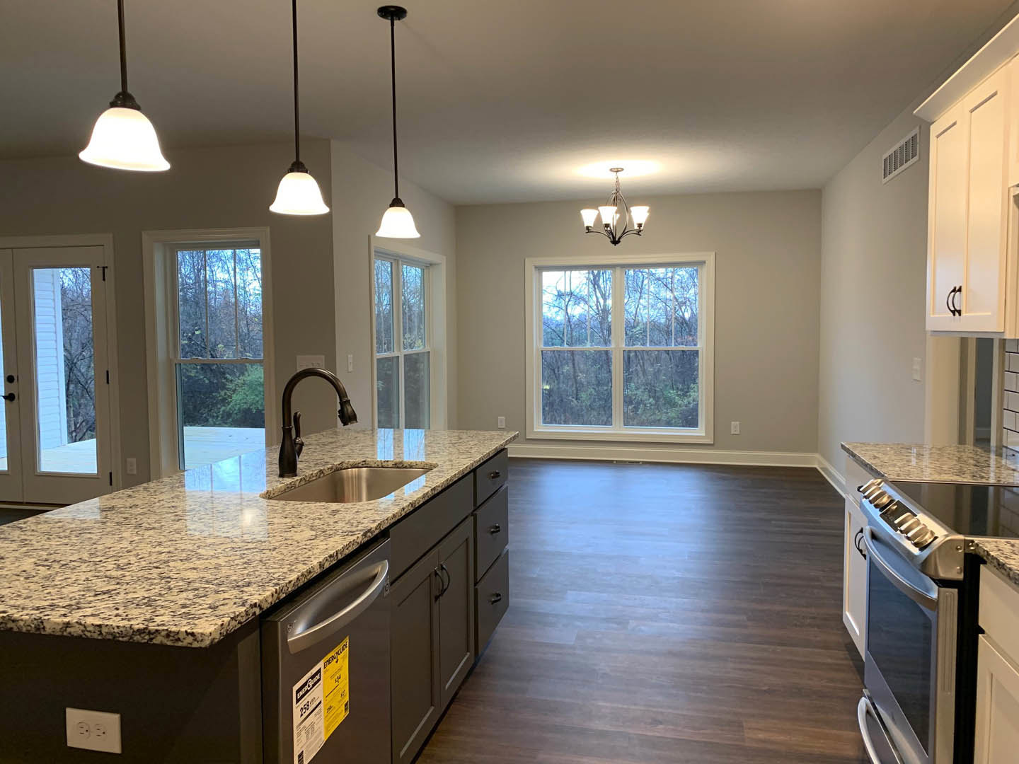 Marble countertop kitchen with wood flooring, white cabinetry, stainless steel refrigerator, modern faucet, decorative chandelier, wall vent, and window overlooking trees