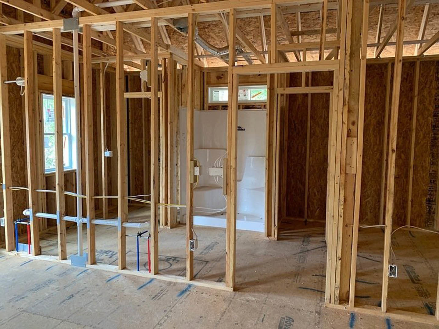 Bathroom under construction with exposed wood framing, shower stall, plumbing pipes, and unfinished ceiling beams