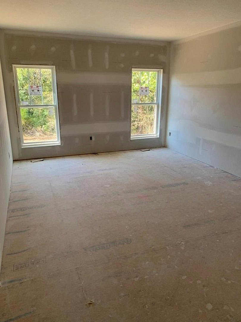 Bright room with two large windows, white plaster walls, light wood flooring, and a door; natural daylight highlights minimalist finishes.