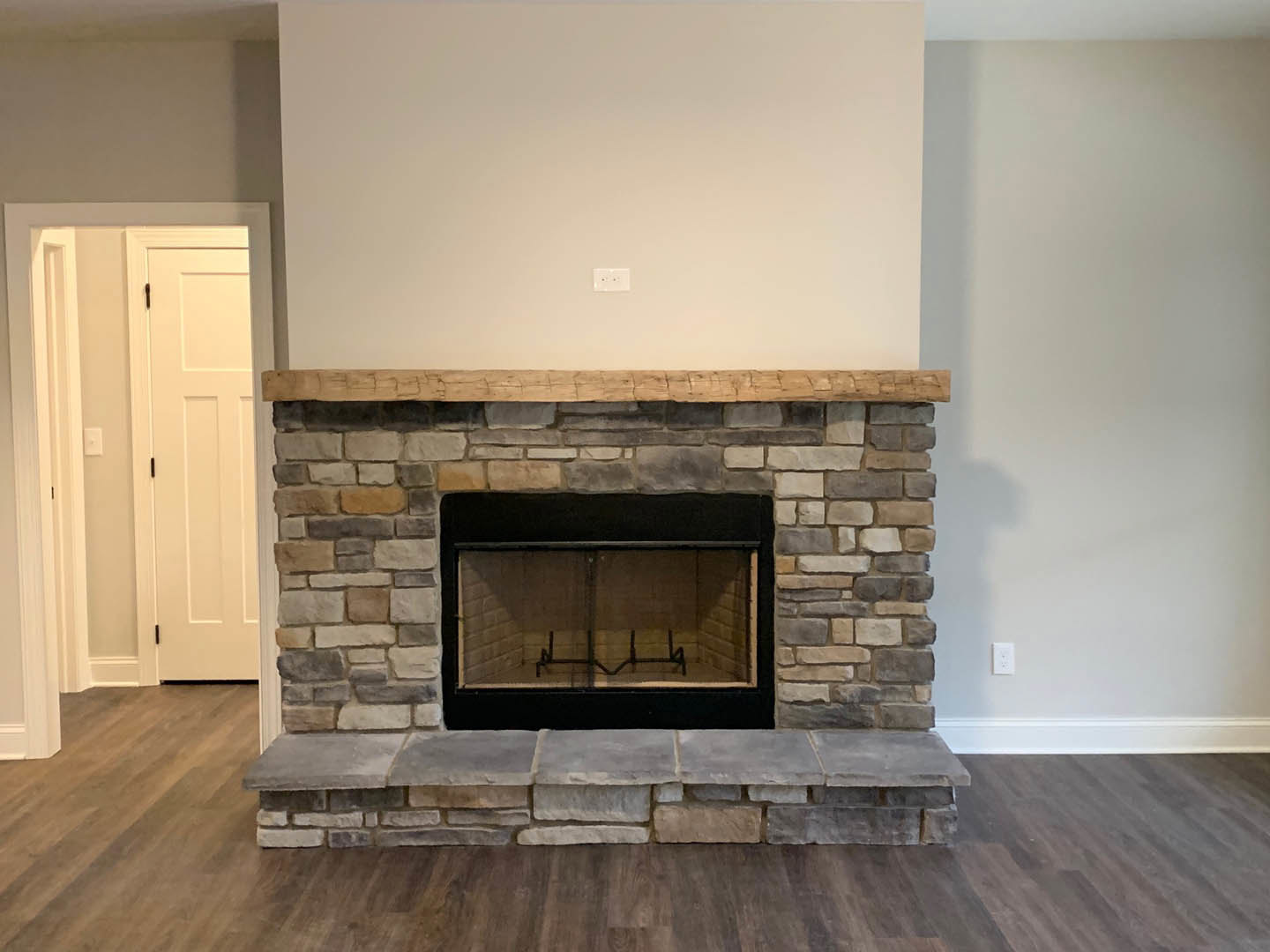 Stone fireplace with glass window and wood frame, black fire screen, white door with black handles, hardwood floor, neutral walls