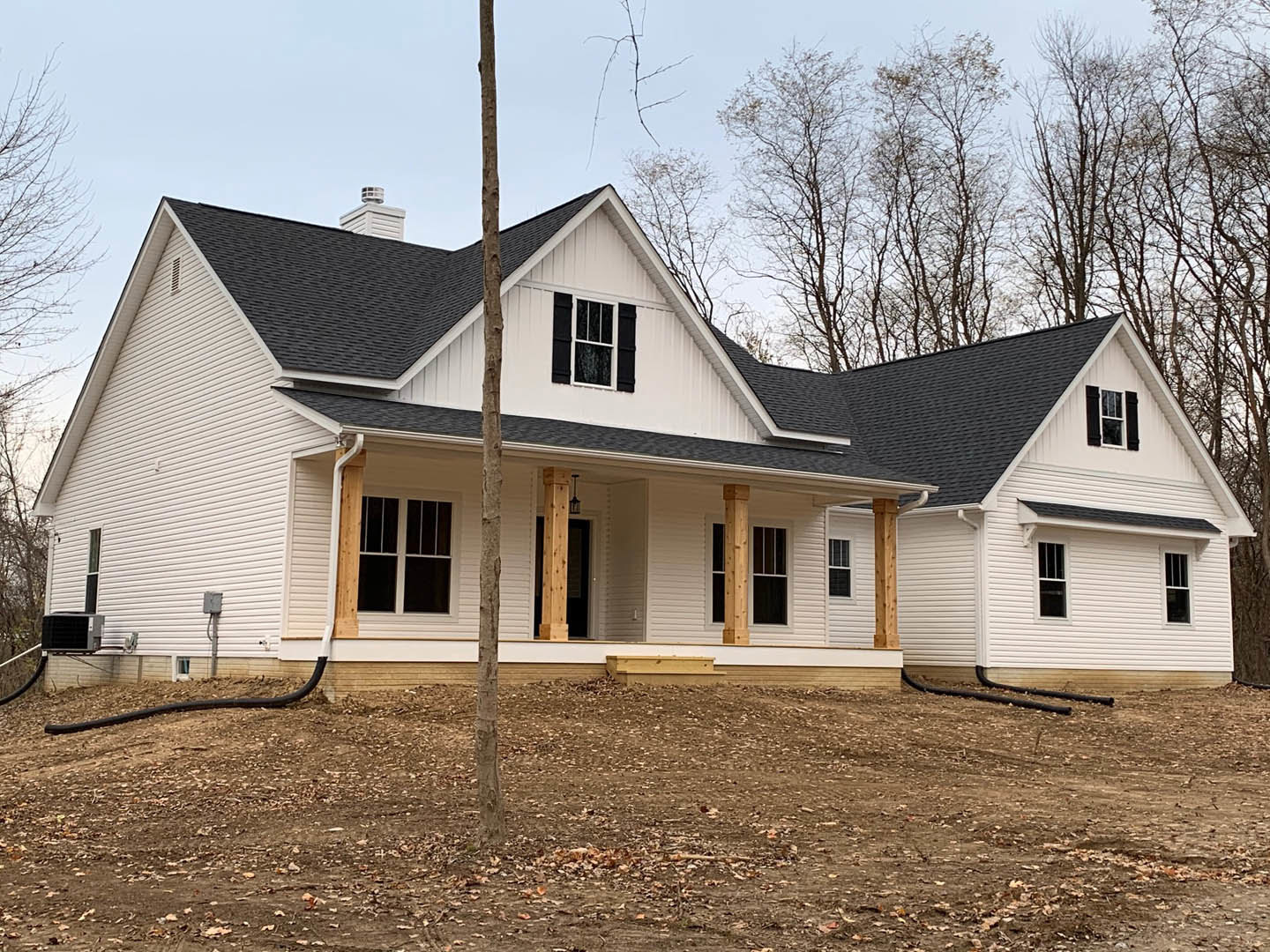 Two-story house with white siding, black shutters, and large windows, set on a spacious yard with scattered leaves and a mature tree in front