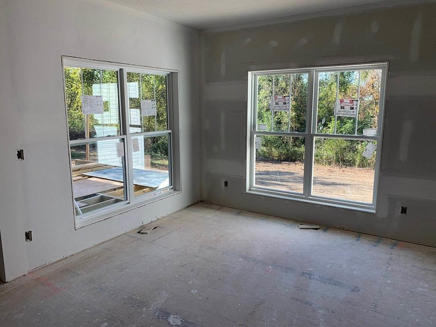Spacious room featuring large windows, smooth concrete flooring, white walls, and a whiteboard with black text.