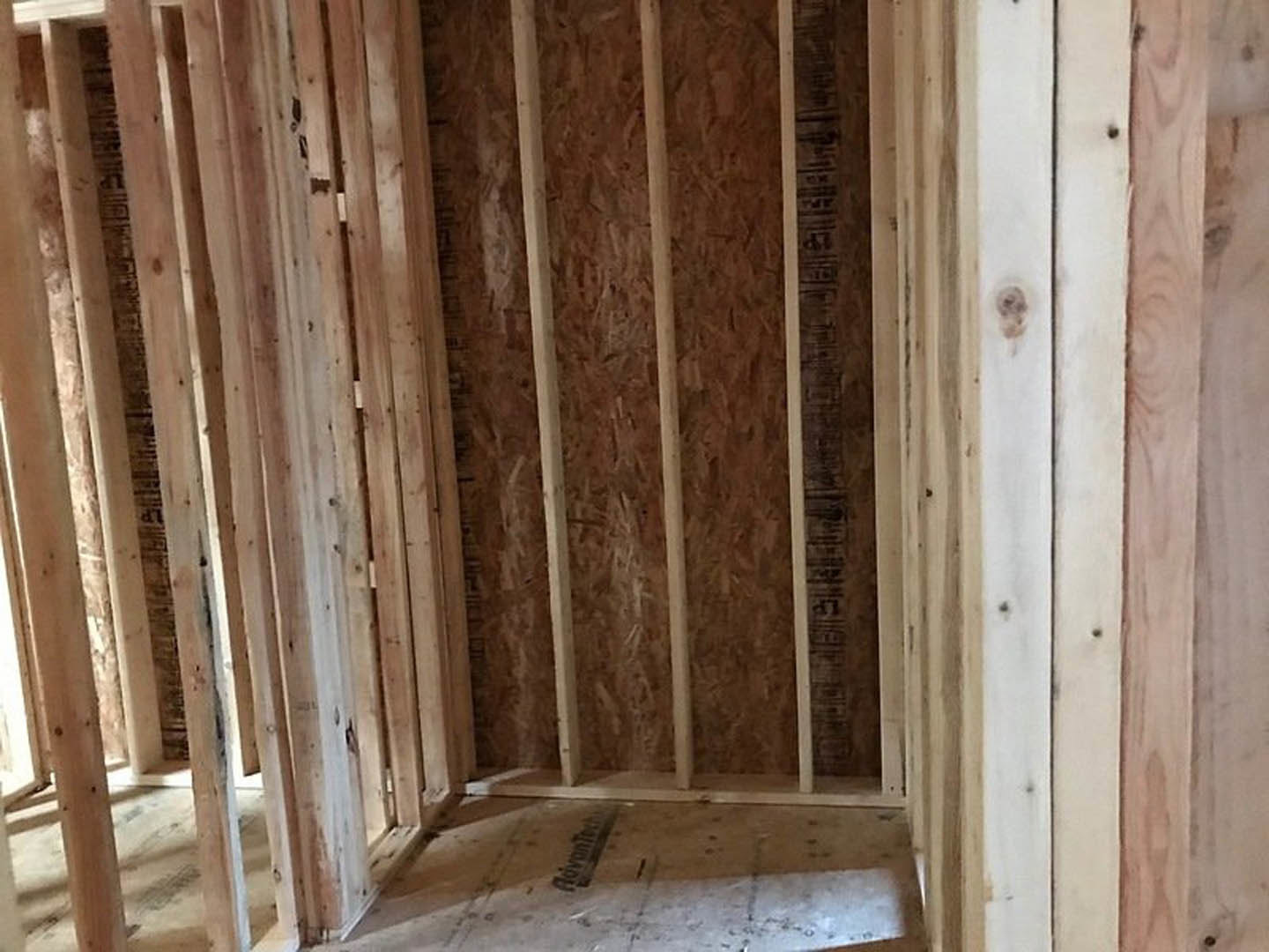 Exposed wood framing and beams in an unfinished room with concrete floor and white wall, highlighting construction materials and interior structure.