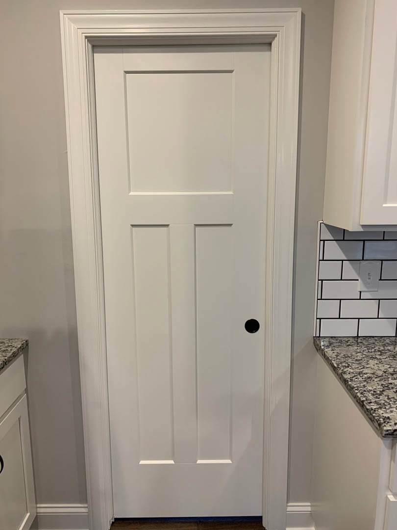 White shaker-style door with black handle beside white subway tile backsplash and light-colored countertop in modern kitchen.