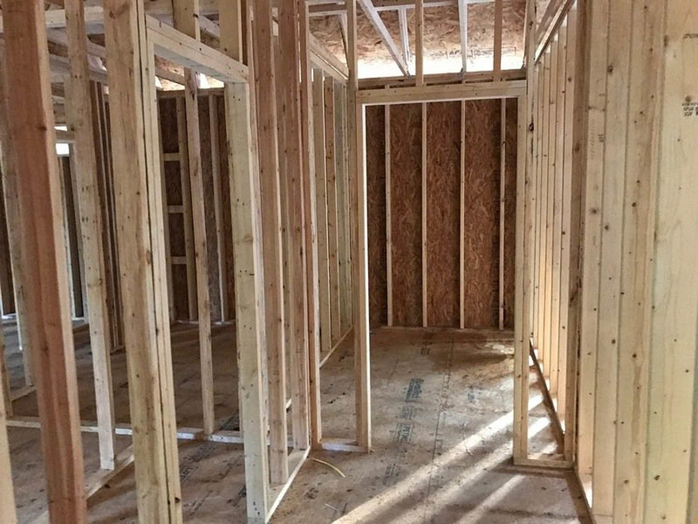 Exposed wood framing with beams and planks, unfinished floor, and visible building insulation in a custom home interior under construction
