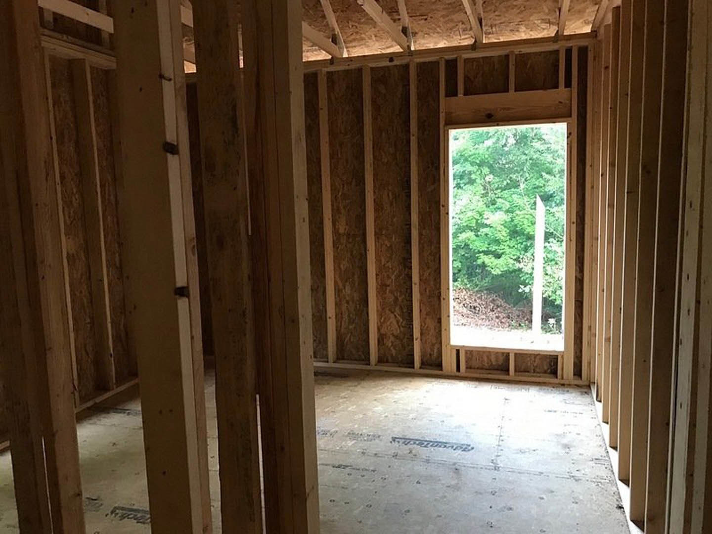 Room with wood-framed window overlooking trees, white door, stone accent wall, concrete floor featuring a logo