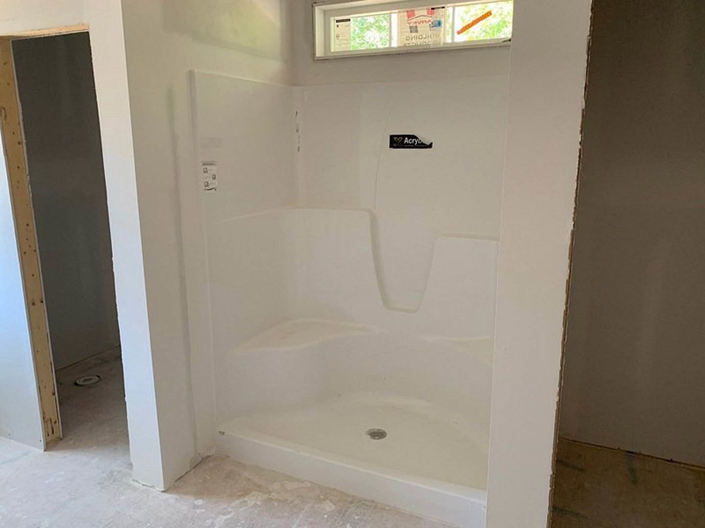 Walk-in shower with white subway tile walls, glass door, chrome fixtures, and built-in drain, adjacent to a window with a sign.
