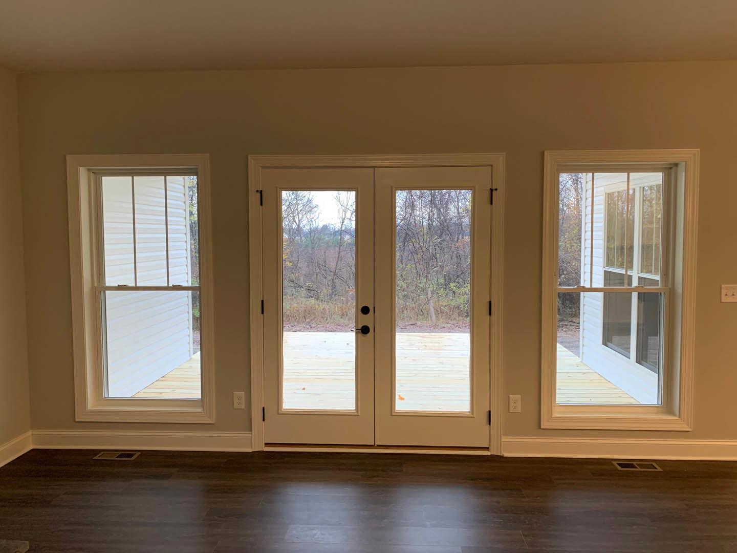 Double doors with glass panes, dark wood flooring, white walls, and windows with white frames