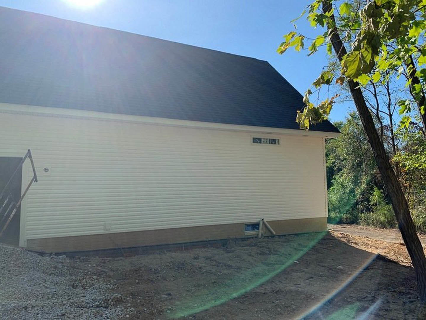 Modern two-story house with black roof, attached garage, white siding, and a large tree in the front yard
