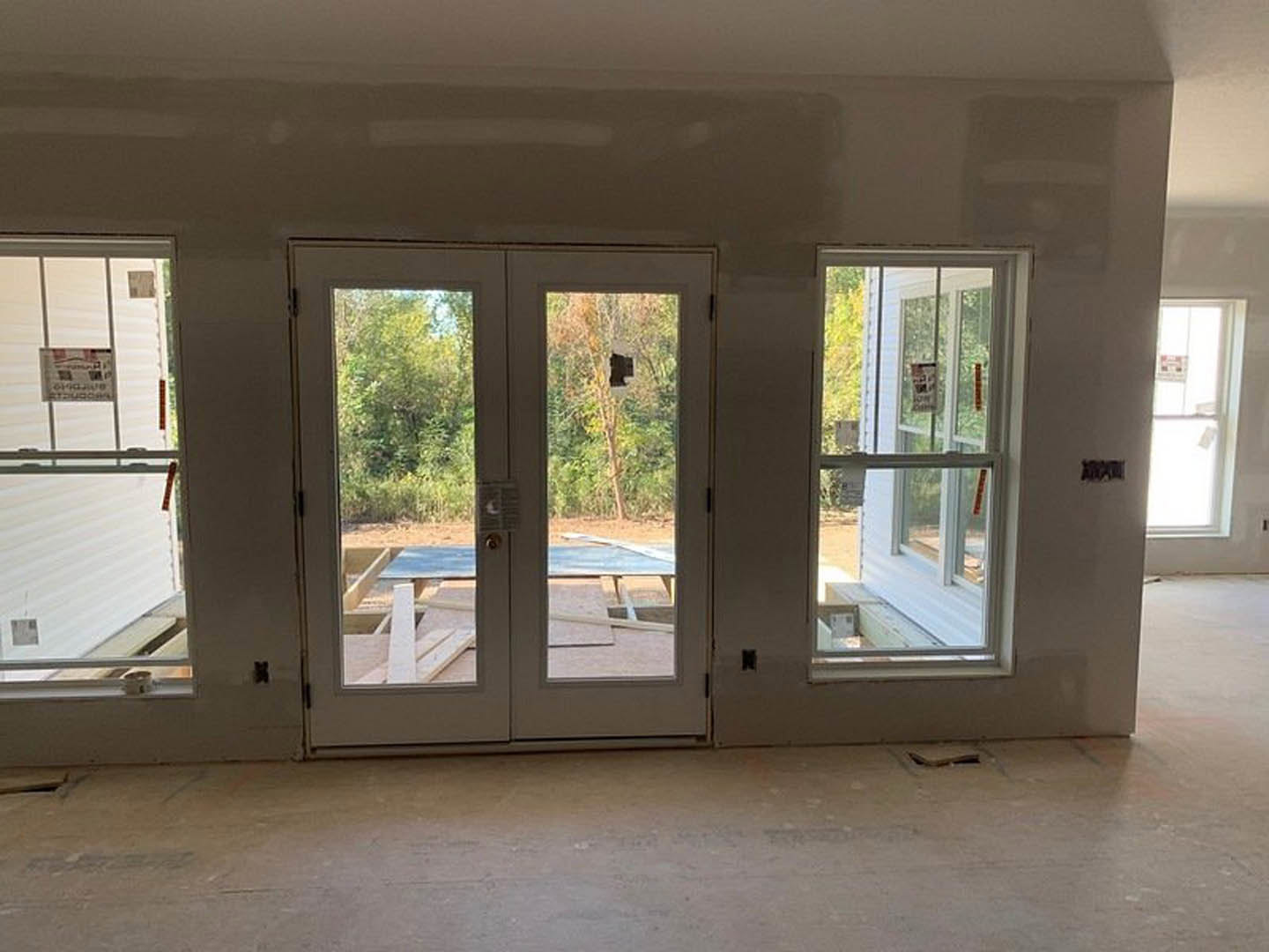 Spacious room featuring double glass doors, large windows with daylight, light-colored flooring, and modern interior finishes; a sign visible on the window and a person blurred in