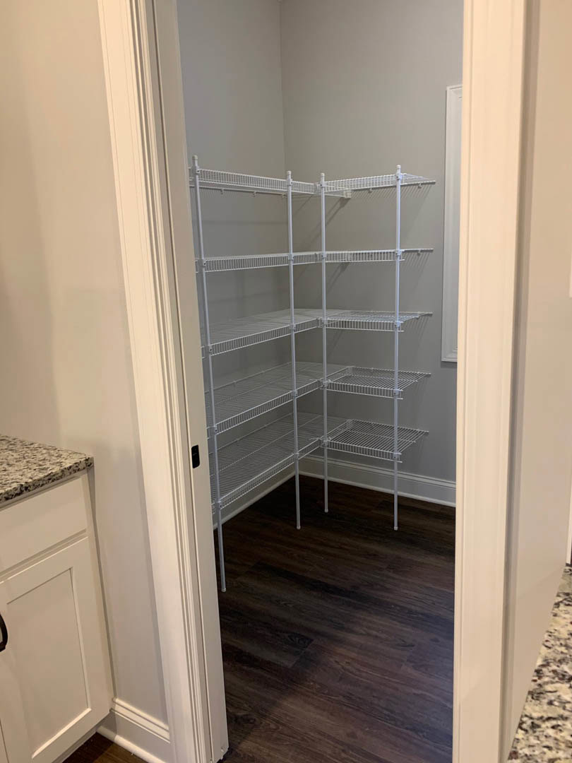 White built-in shelves against a wall, wood flooring, white door with black handle, white cabinetry and countertop in a modern room