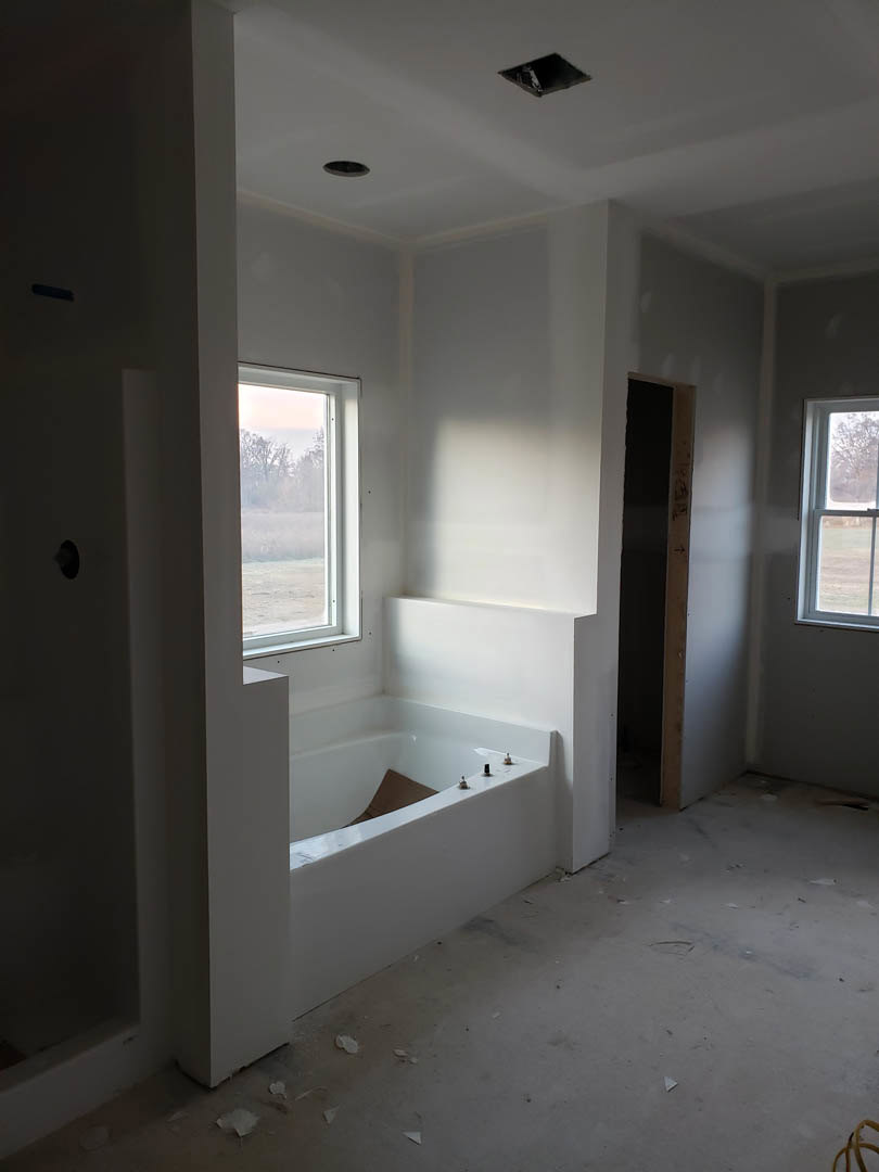 White bathroom with freestanding soaking tub beneath large window, light plaster walls, wood flooring, and chrome fixtures