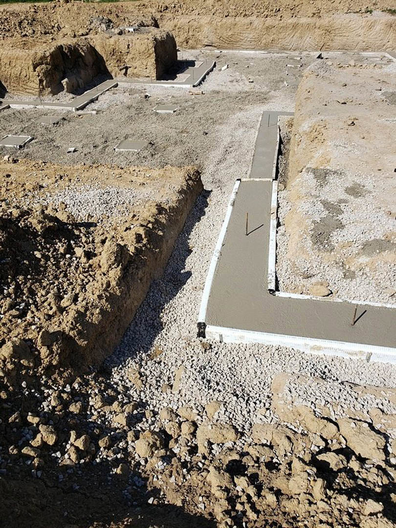 Concrete foundation slab with embedded metal rods at residential construction site, surrounded by exposed soil and rocks