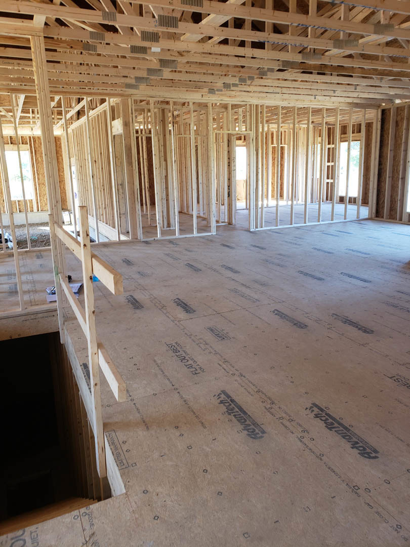 Open living space with exposed wood ceiling beams, wood plank flooring, and a metal ladder leaning against the wall