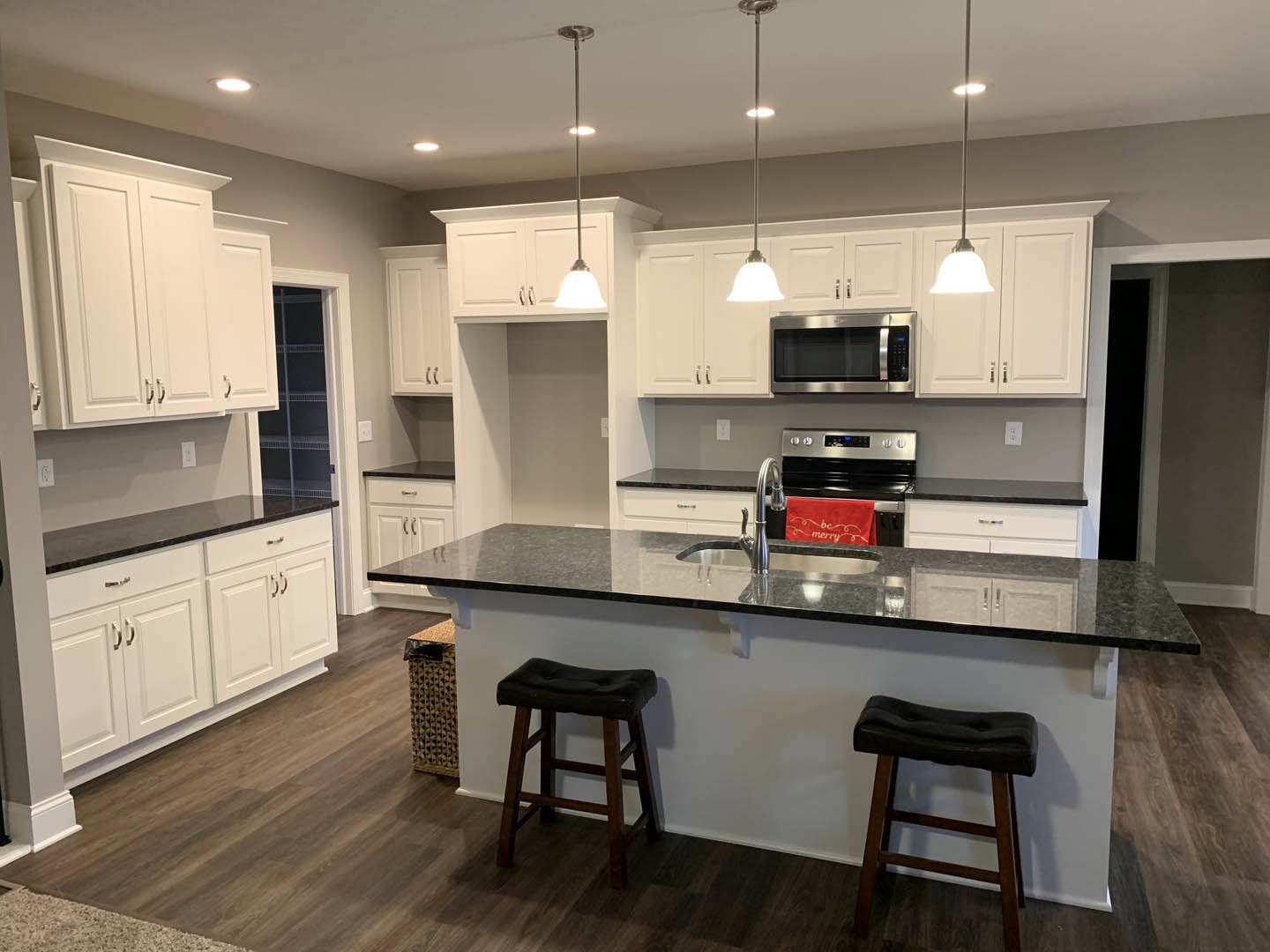 White kitchen cabinets with black countertops, stainless steel microwave, black leather bar stool, cushioned stool, red towel draped over stove, light walls and flooring