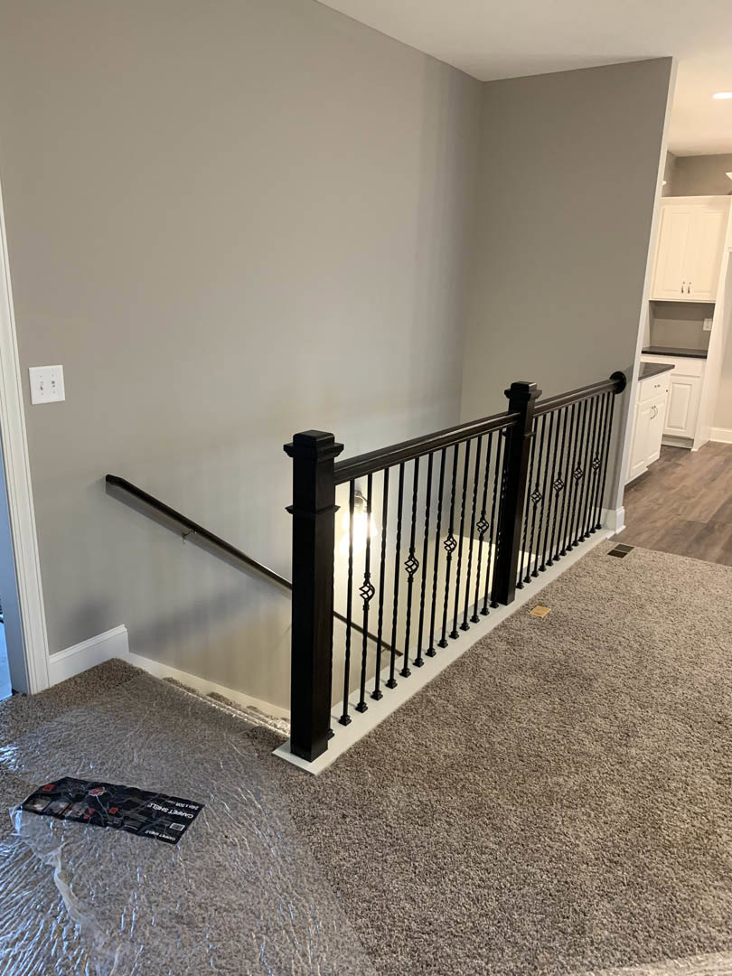 Staircase with black metal railing, white walls, carpeted floor, white light switch, and black rectangular decorative object on wall