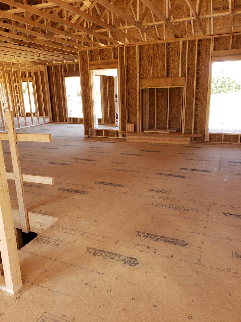 Open living space with exposed wood ceiling beams, wide plank wood flooring, and large windows overlooking green trees