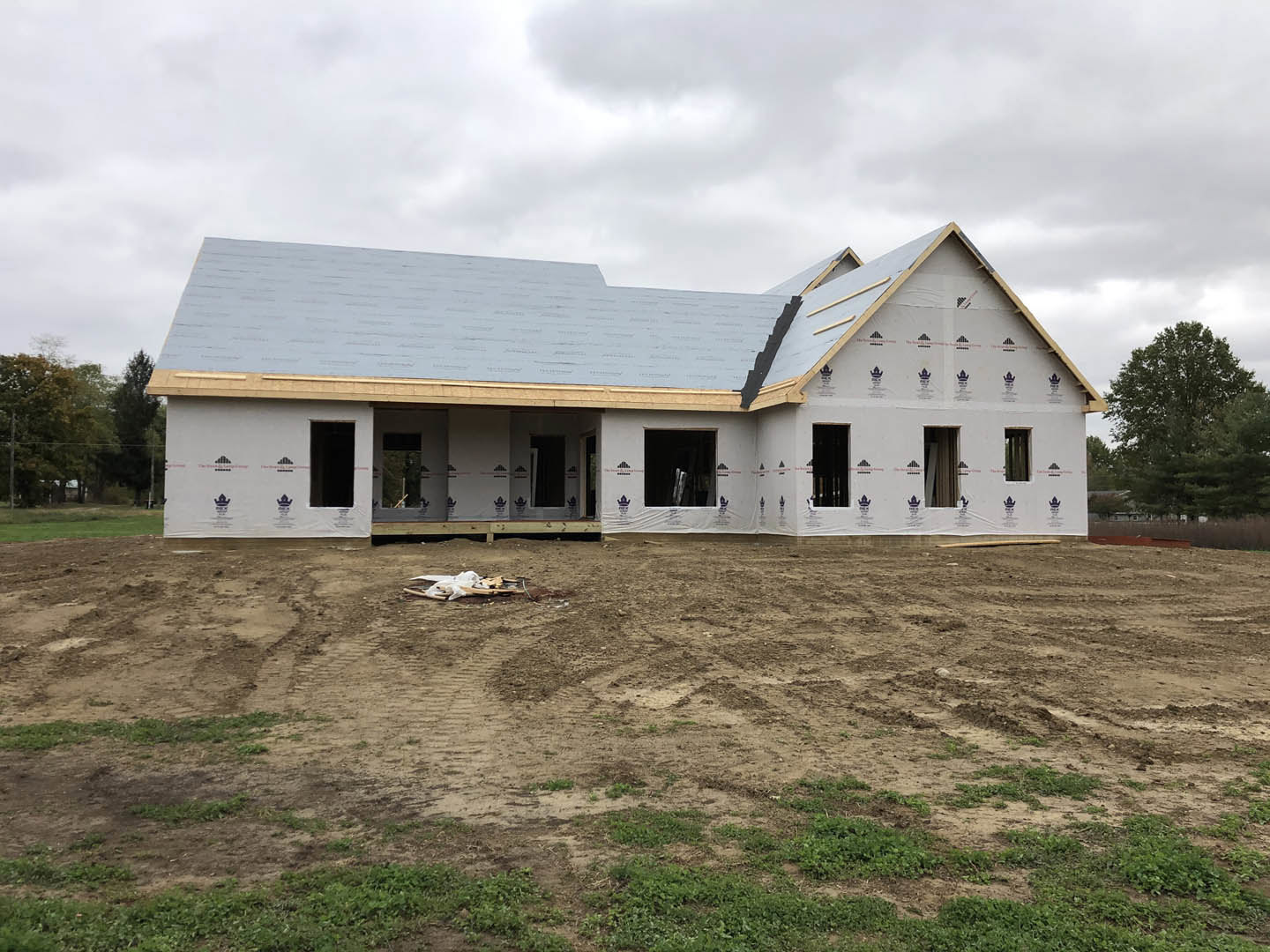 Partially built house with grey roof, surrounded by dirt and grass, construction debris in foreground, Robert Frost Farm visible in background, cloudy sky overhead, window