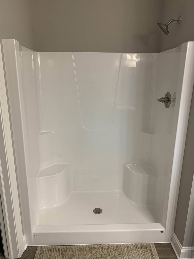 White tile shower with chrome showerhead, glass door, and built-in niche in modern bathroom.