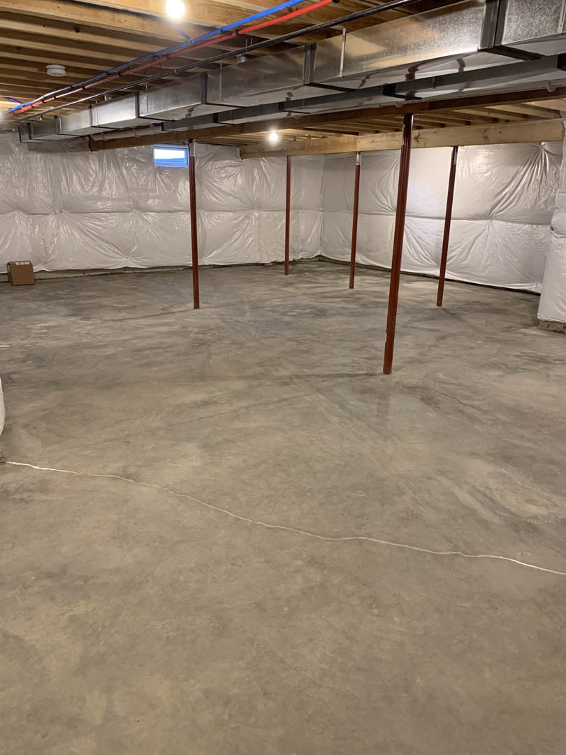 Concrete basement floor with white plastic coverings, exposed wood post, metal vent, and ceiling light