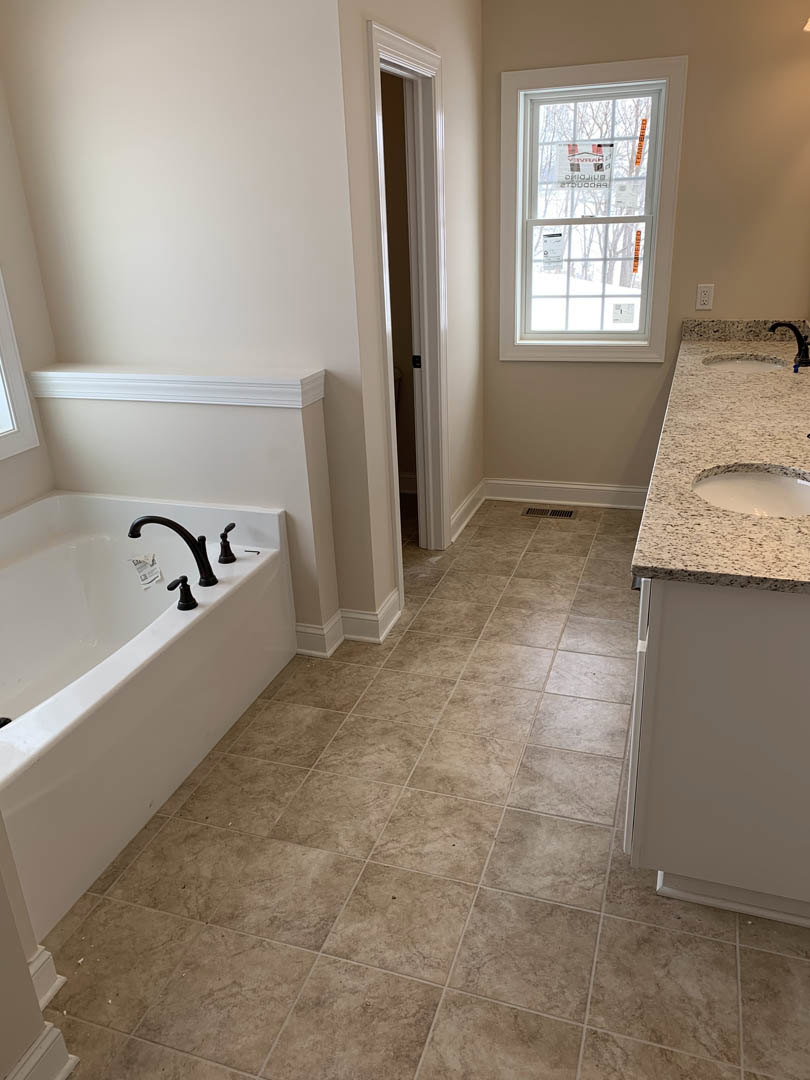Bathroom with white tile floor, freestanding bathtub with chrome edge-mounted faucets, white sink set on countertop, window above tub displaying a sign.