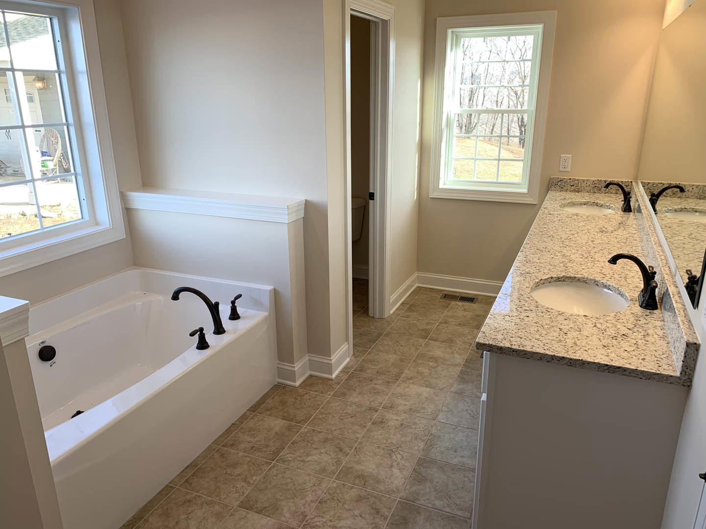 Bathroom with freestanding tub, white sink on black speckled countertop, tile floor, large window overlooking trees, chrome faucets, neutral walls
