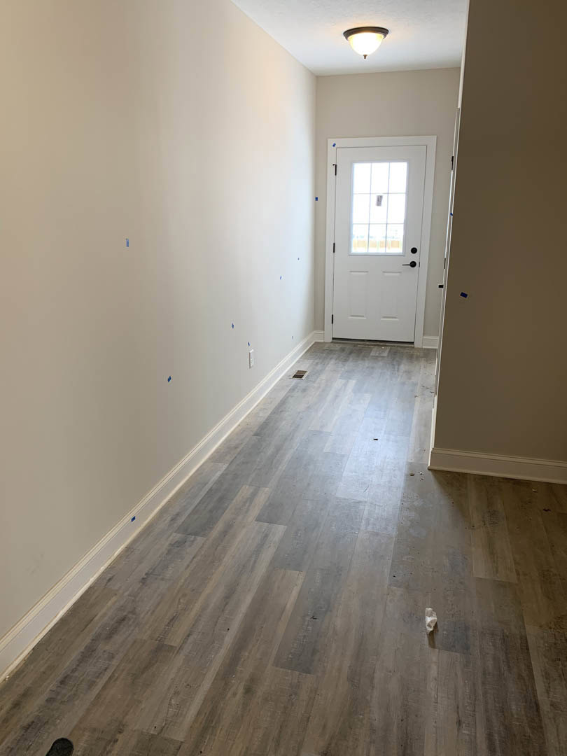 Hallway with light wood flooring, white plaster walls, white door featuring a glass window, round ceiling light fixture, blue painter’s tape on wall