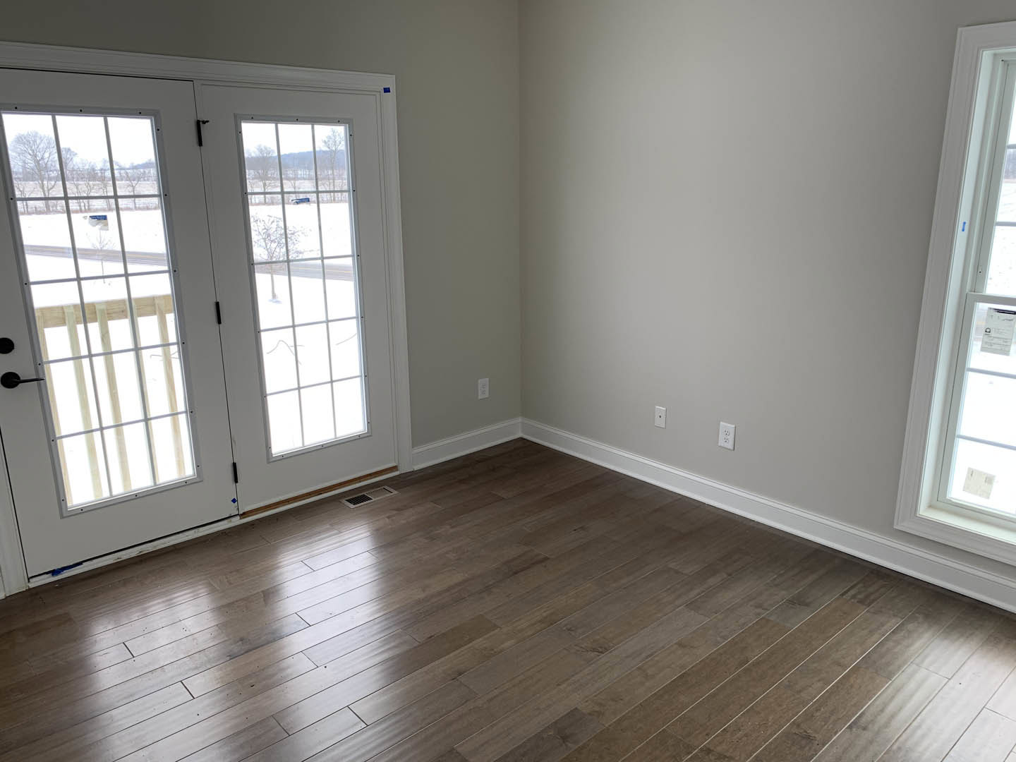 Wood flooring in a bright room, glass-paneled door leading to outdoor deck, white walls, large window, modern interior finishes
