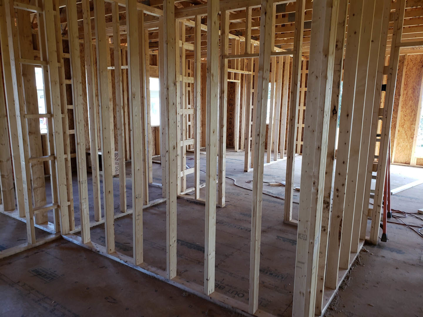 Exposed wood framing and beams inside a partially constructed residential room, unfinished floor, natural light highlighting construction materials