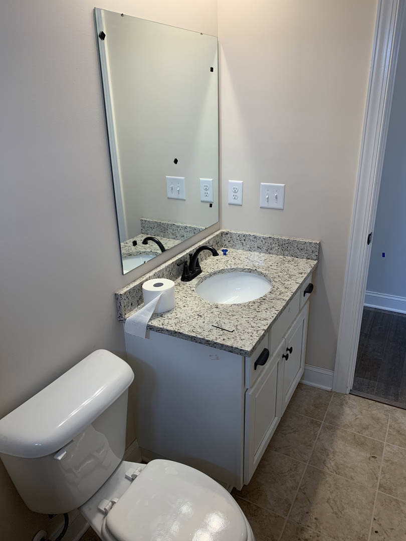 Modern bathroom with white toilet, rectangular sink on marble countertop, wall-mounted mirror, chrome faucet, light tile flooring, and toilet paper holder