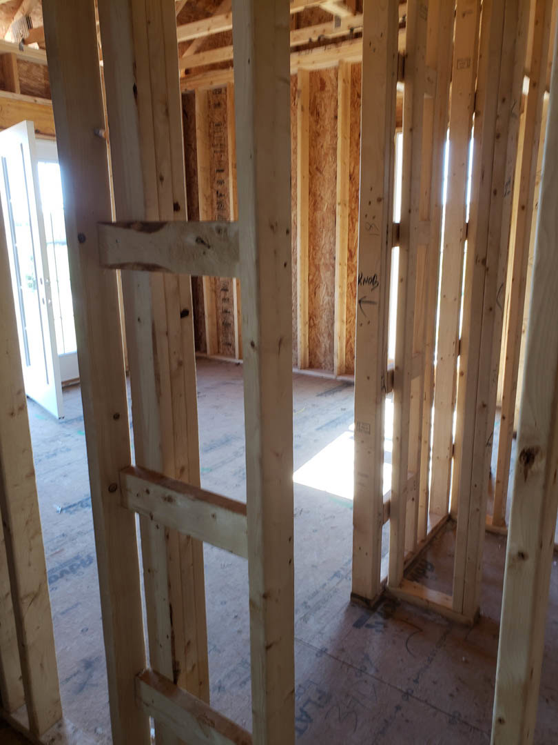 Exposed wood framing and beams in an unfinished room with visible lumber, planks, and a window opening