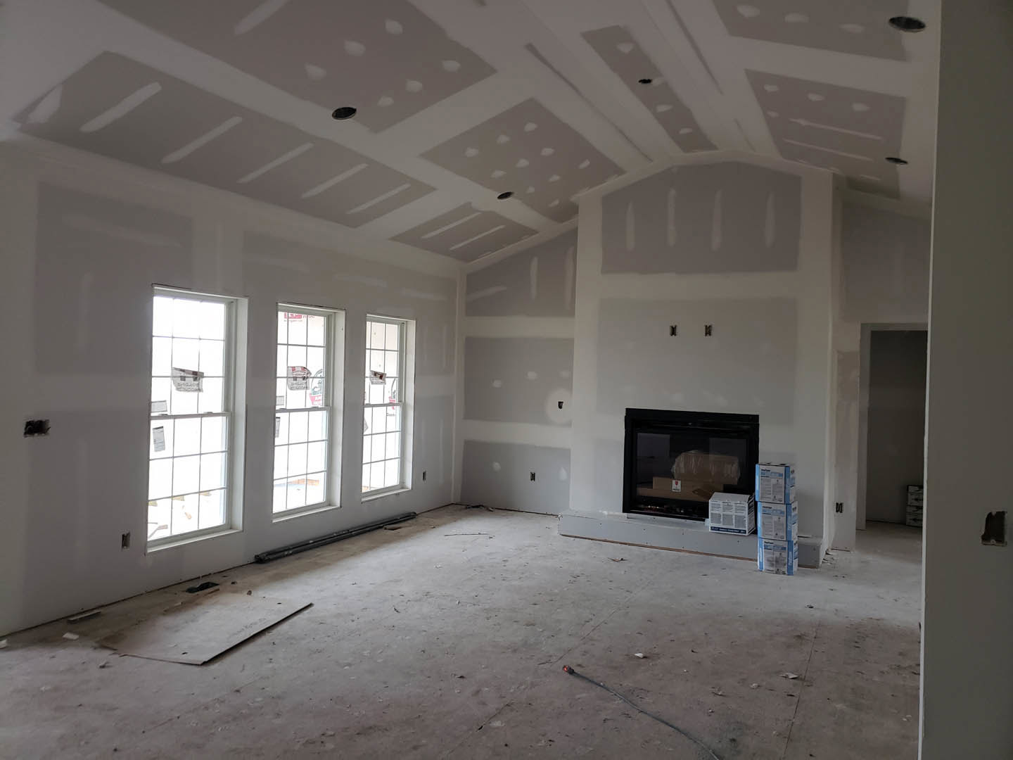 Living room with plaster walls, large windows, wood floor, and modern fireplace with stacked firewood inside