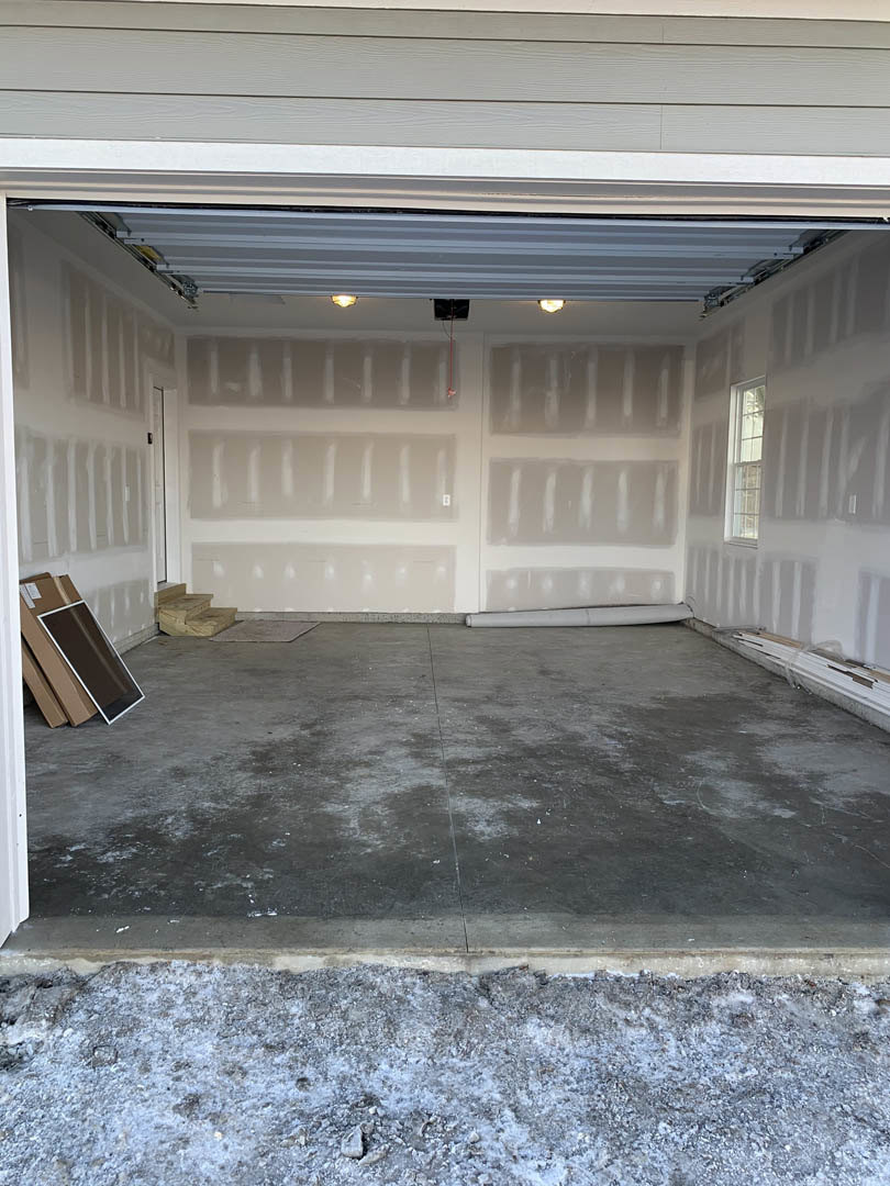 Garage interior with concrete floor, plaster walls, and composite ceiling, featuring a closed garage door