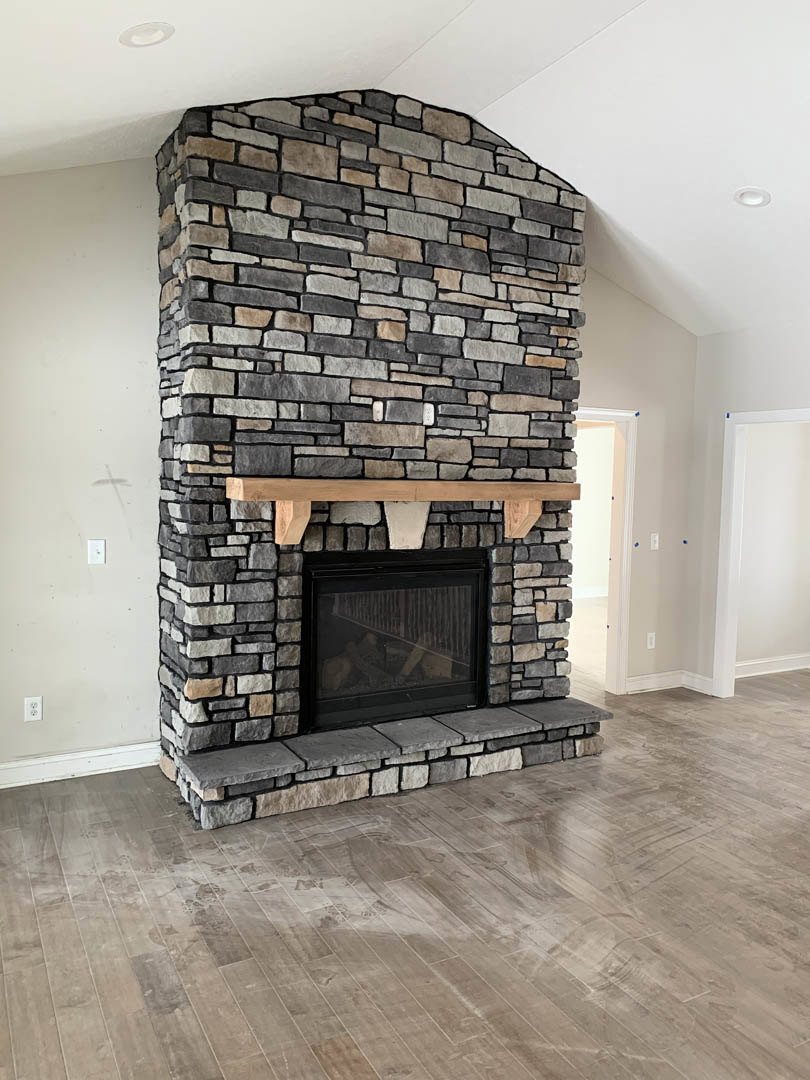 Stone fireplace with glass door and wood mantel, set against a white wall with adjacent white door, wood flooring, and fire screen.