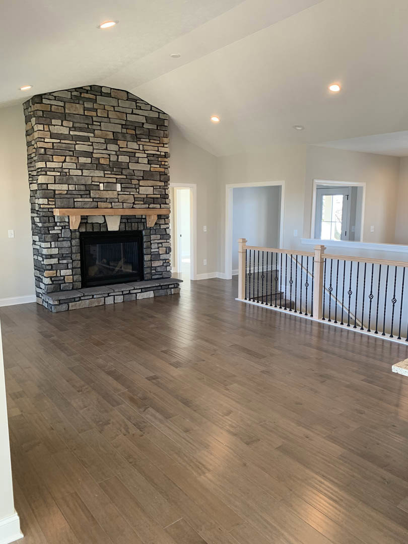 Living room featuring a stone fireplace with glass doors, wood mantle, hardwood flooring, staircase close-up, and a white door with glass panes