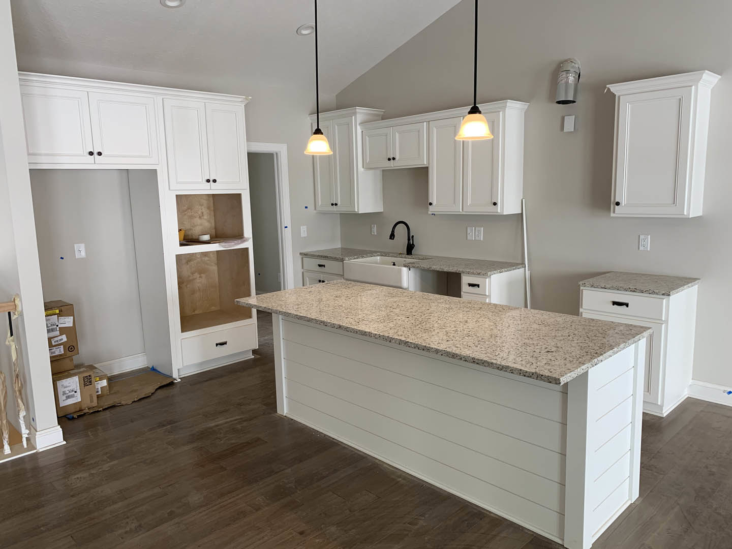 Spacious kitchen featuring a large central island with marble countertop, white cabinetry, tile backsplash, stainless steel sink and faucet, and light wood flooring