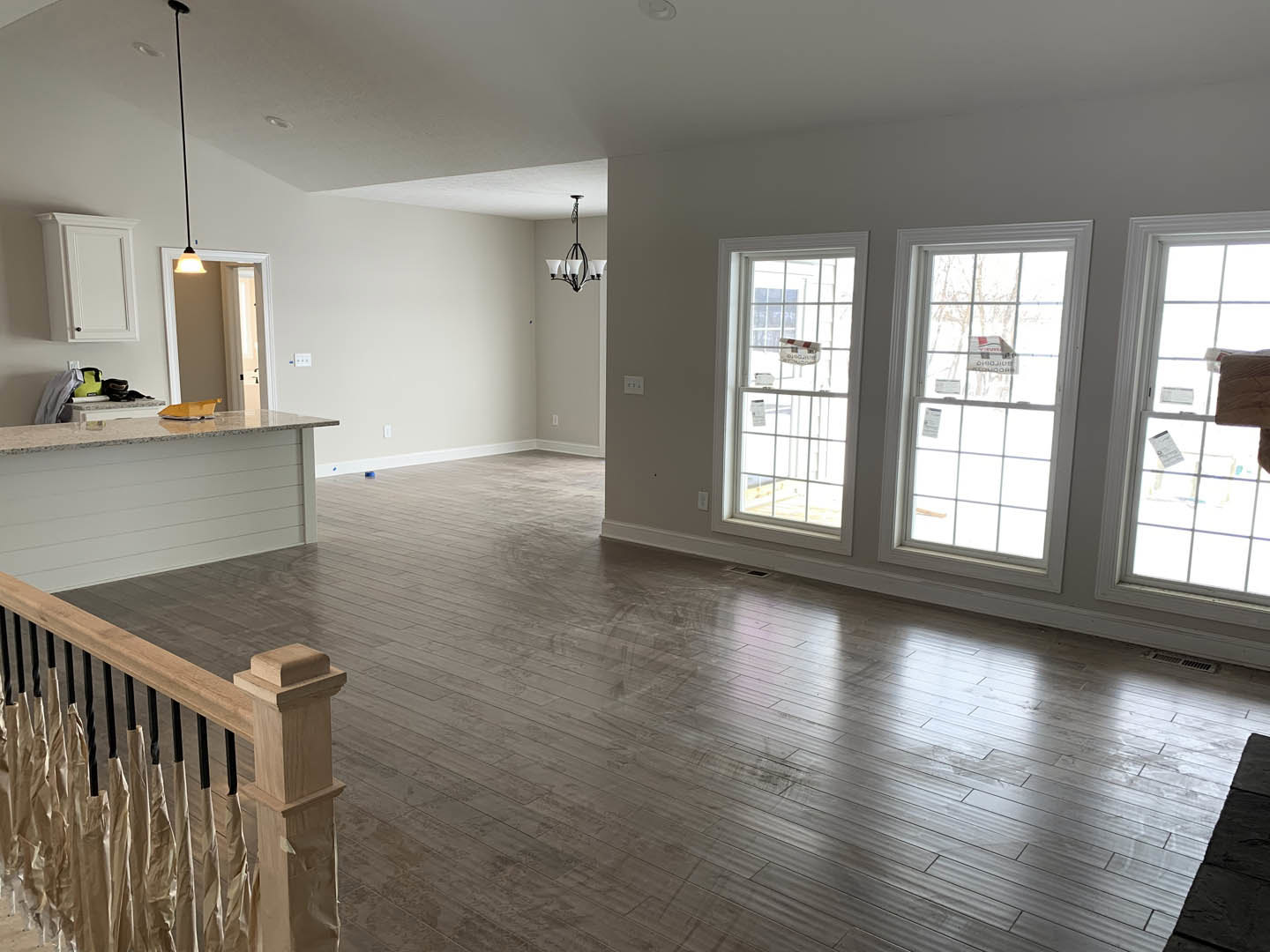 Open living area with hardwood floors, white walls, wood staircase with metal railing, large windows letting in natural light, woven basket placed on windowsill
