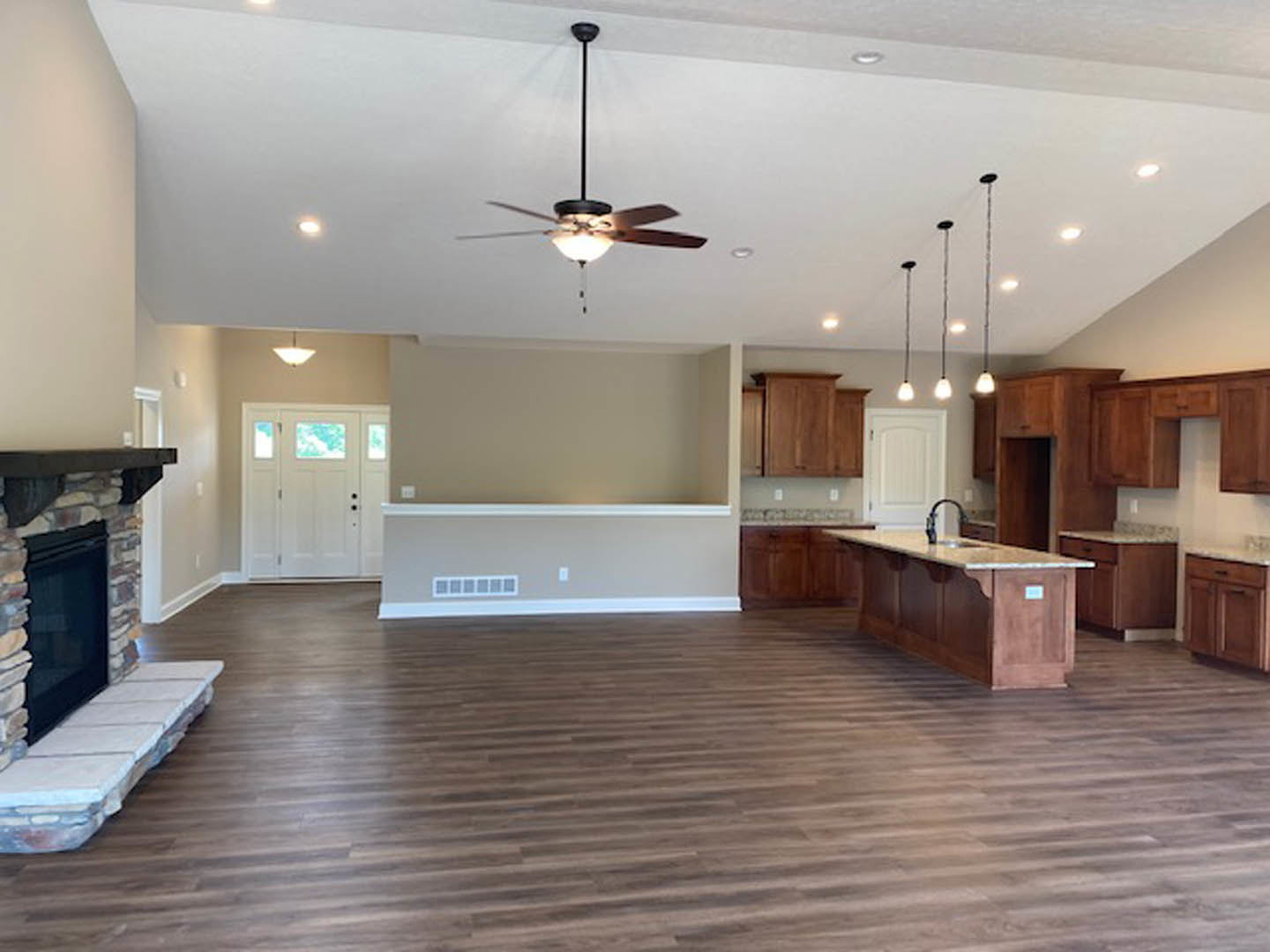 Spacious open floor plan featuring hardwood flooring, central kitchen island with sink, white cabinetry, a dog bed near the island, and a white door with three windows.
