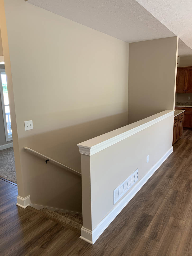 Hardwood staircase with white railing, white plaster walls featuring a vent and light switch, window allowing natural light into the room