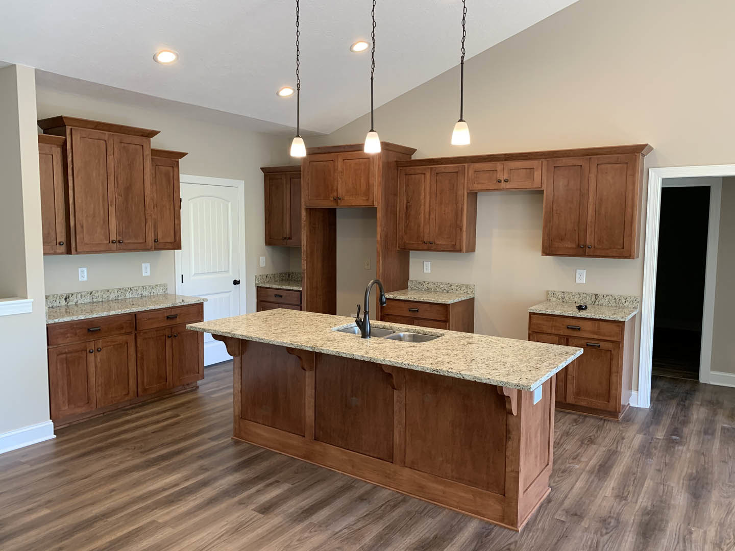 Spacious kitchen featuring a large granite island with built-in sink, white cabinetry with black handles, wooden cabinet accents, and contrasting black and white doors.