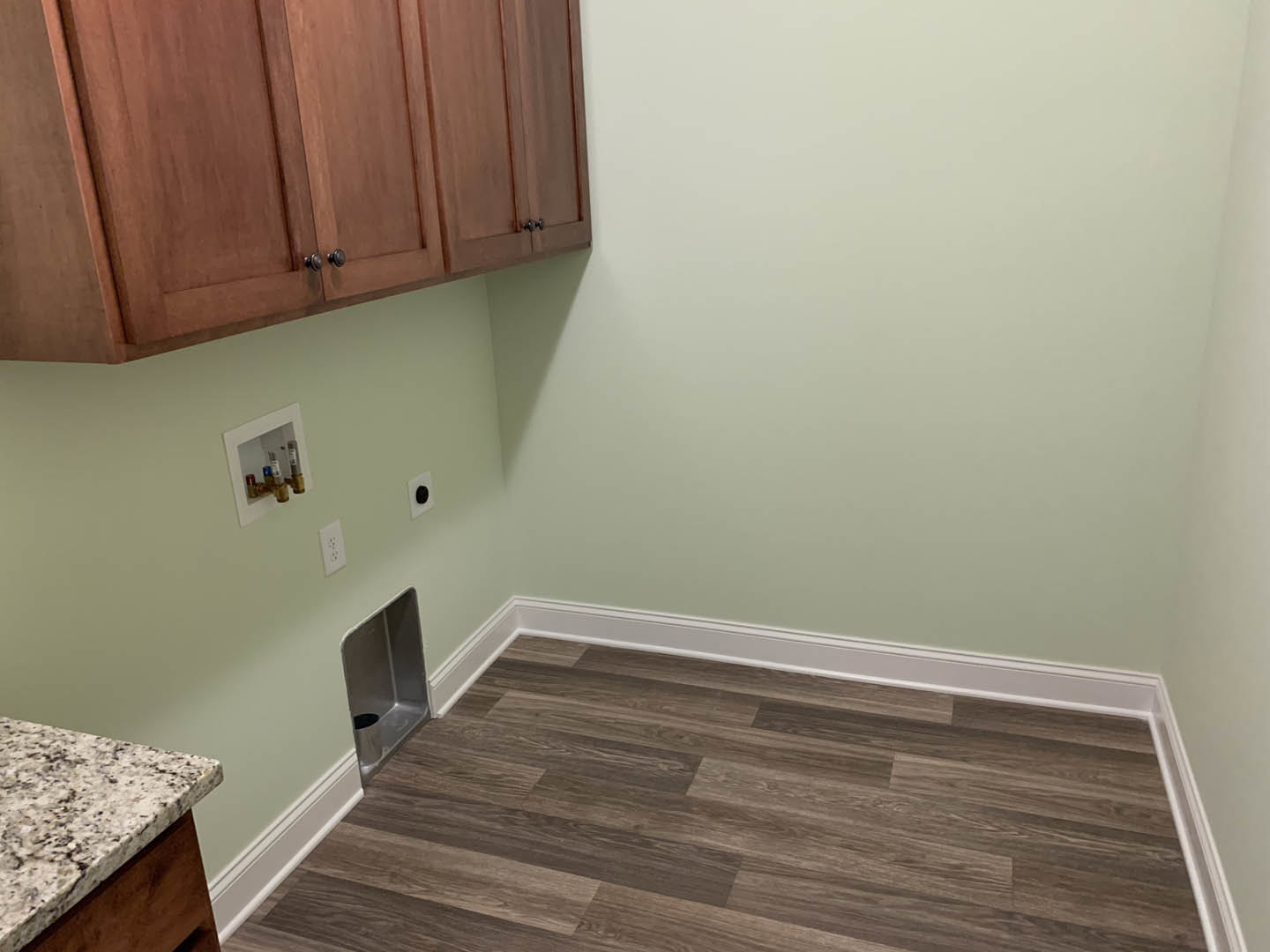Open kitchen with wood flooring, light wood cabinets with metal knobs, white baseboards, and a stone countertop